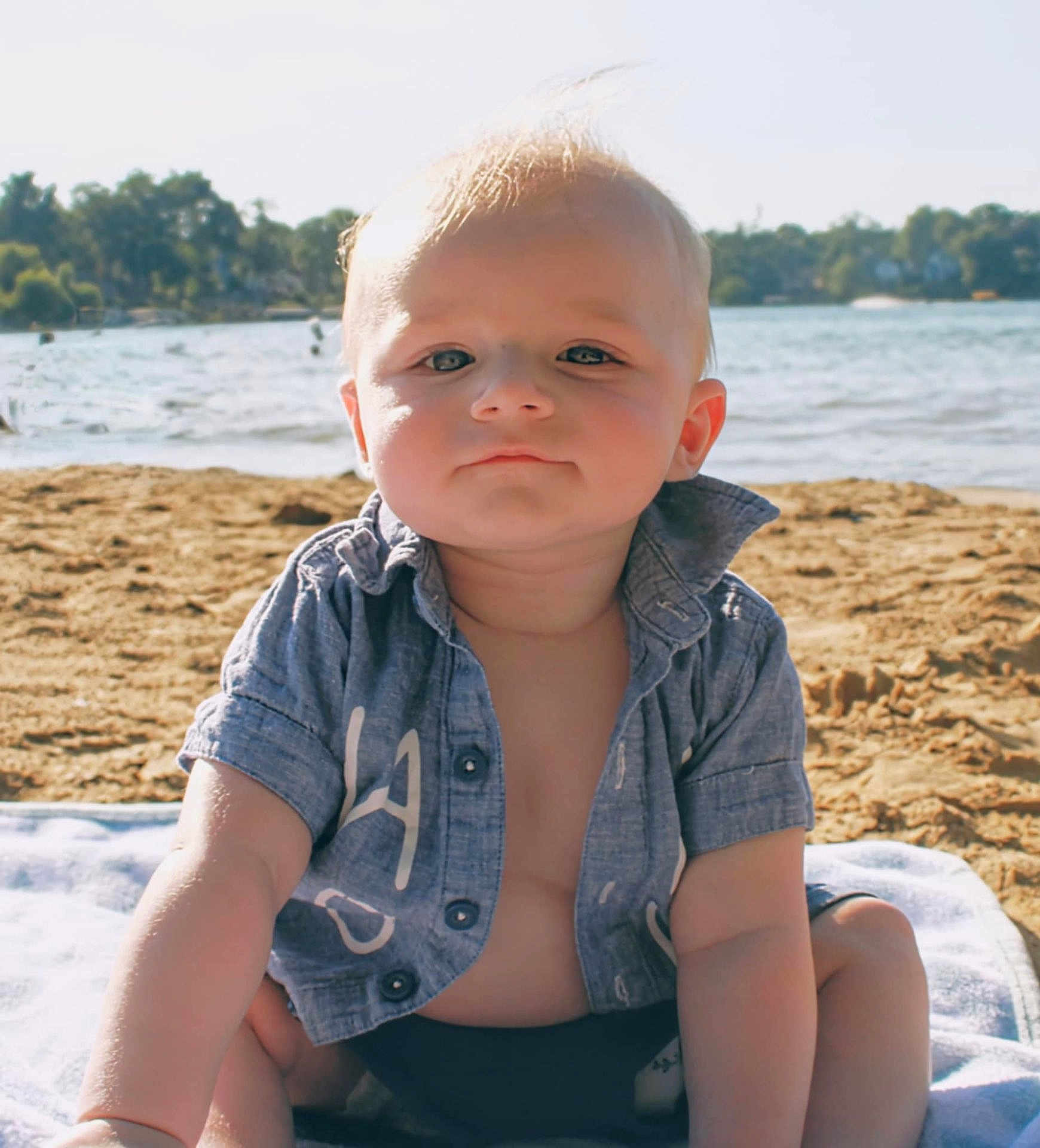 Ezra joined the competition — help win amazing prizes! baby, child, beach, sand, water, towel, shirt, sunlight, outdoor, summer, portrait, blue_shirt, swimwear, sitting, face, cute, young_child, nature, daytime, vacation