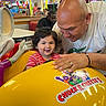 toddler, child, adult, arcade, indoor, ride, yellow, smile, happy, curly_hair, red_striped_shirt, entertainment, family, fun, play, colorful, game_center, Chuck_E_Cheese, people, interaction