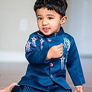 Thiansh joined the competition — help win amazing prizes! toddler, child, boy, blue_outfit, indoor, floor, kneeling, cute, portrait, face, hair, playful, expression, buttoned_jacket, embroidery, barefoot, young, person, smiling, skin