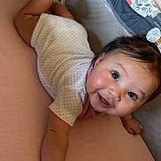 Penelope is registered to the contest to win money with this photo: baby, smiling, face, arm, hand, bracelet, hair_bow, white_clothing, polka_dots, pink_mattress, lying_down, indoors, happy, cute, child, infant, skin, person, closeup, portrait