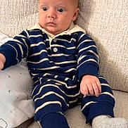 Theodore is registered to the contest to win money with this photo: baby, child, striped_clothing, navy_blue, white, onesie, couch, beige, texture, sitting, sock, infant, portrait, indoor, face, expression, furniture, curious, young_child, person