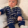 baby, child, striped_clothing, navy_blue, white, onesie, couch, beige, texture, sitting, sock, infant, portrait, indoor, face, expression, furniture, curious, young_child, person
