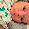 baby, infant, face, onesie, dinosaur_pattern, blue_eyes, lying_down, cute, newborn, child, skin, head, clothing, bed, blanket, indoors, portrait, expression, closeup, person