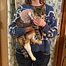 Zelda is registered to the contest to win money with this photo: cat, person, indoor, blue_sweater, tabby_cat, tutu, floral_curtains, wooden_door, holding, clothing, jeans, hand, pet, animal, home, portrait, feline, casual, cute, domestic