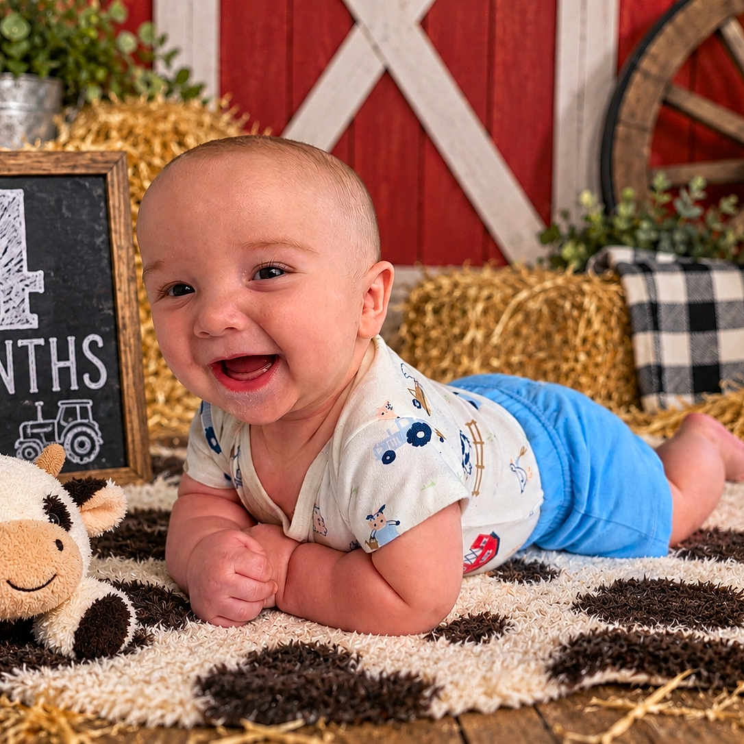 Anthony joined the competition — help win amazing prizes! baby, infant, child, smiling, happy, portrait, farm_theme, barn, hay, plush_toy, cow_toy, rug, chalkboard, four_months, wagon_wheel, milk_can, red_background, sitting, indoor, photography