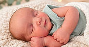 Anthony joined the competition — help win amazing prizes! newborn, baby, sleeping, infant, portrait, close_up, blanket, cozy, indoors, warm_lighting, peaceful, curled_up, green_outfit, knitwear, face, hands, closed_eyes, nursery, bokeh, photography