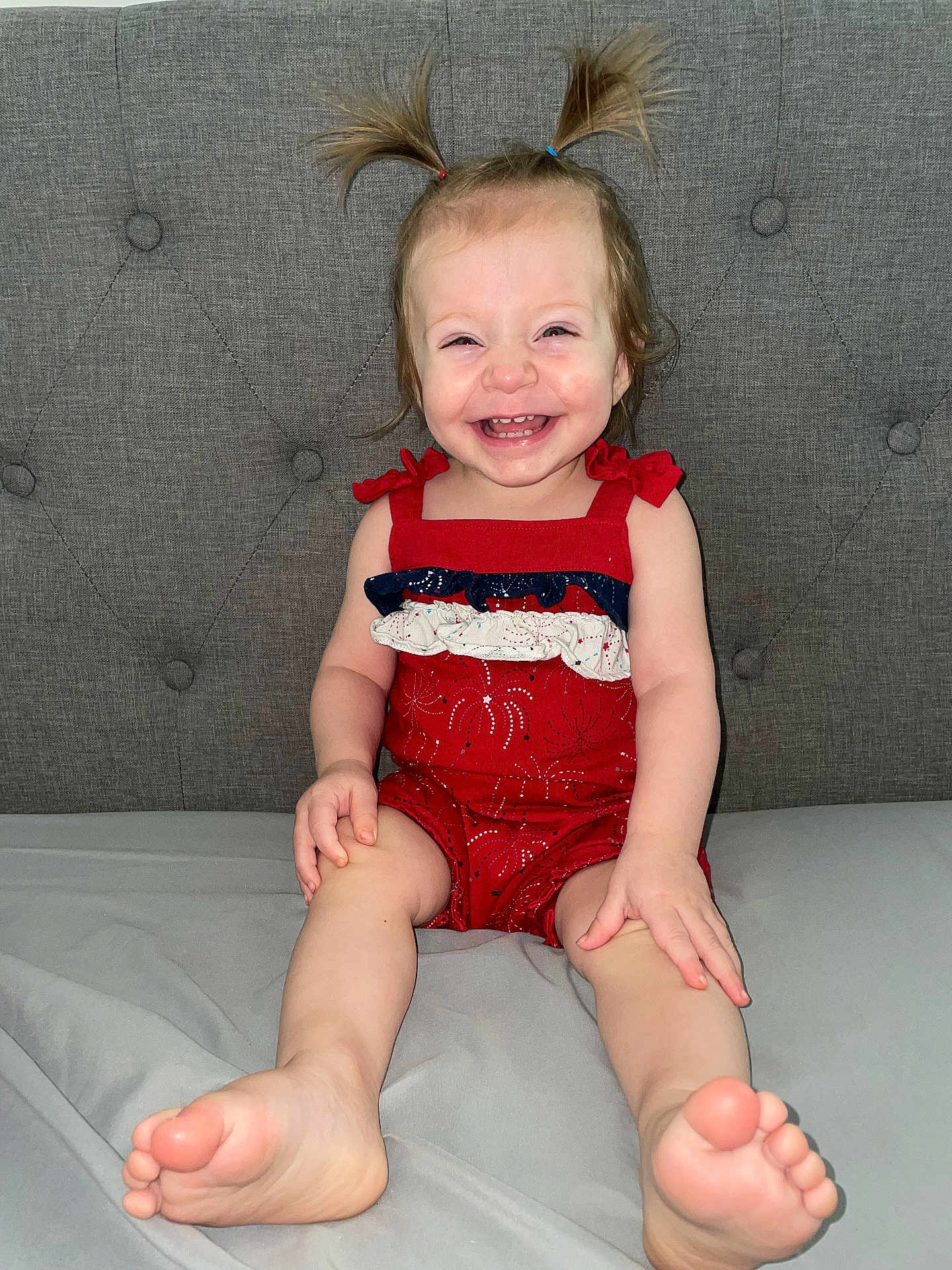 Paisley is registered to the contest to win money with this photo: toddler, child, smiling, happy, sitting, pigtails, red_outfit, clothing, barefoot, feet, face, person, indoor, couch, gray_couch, fabric, cute, young_child, portrait, playful
