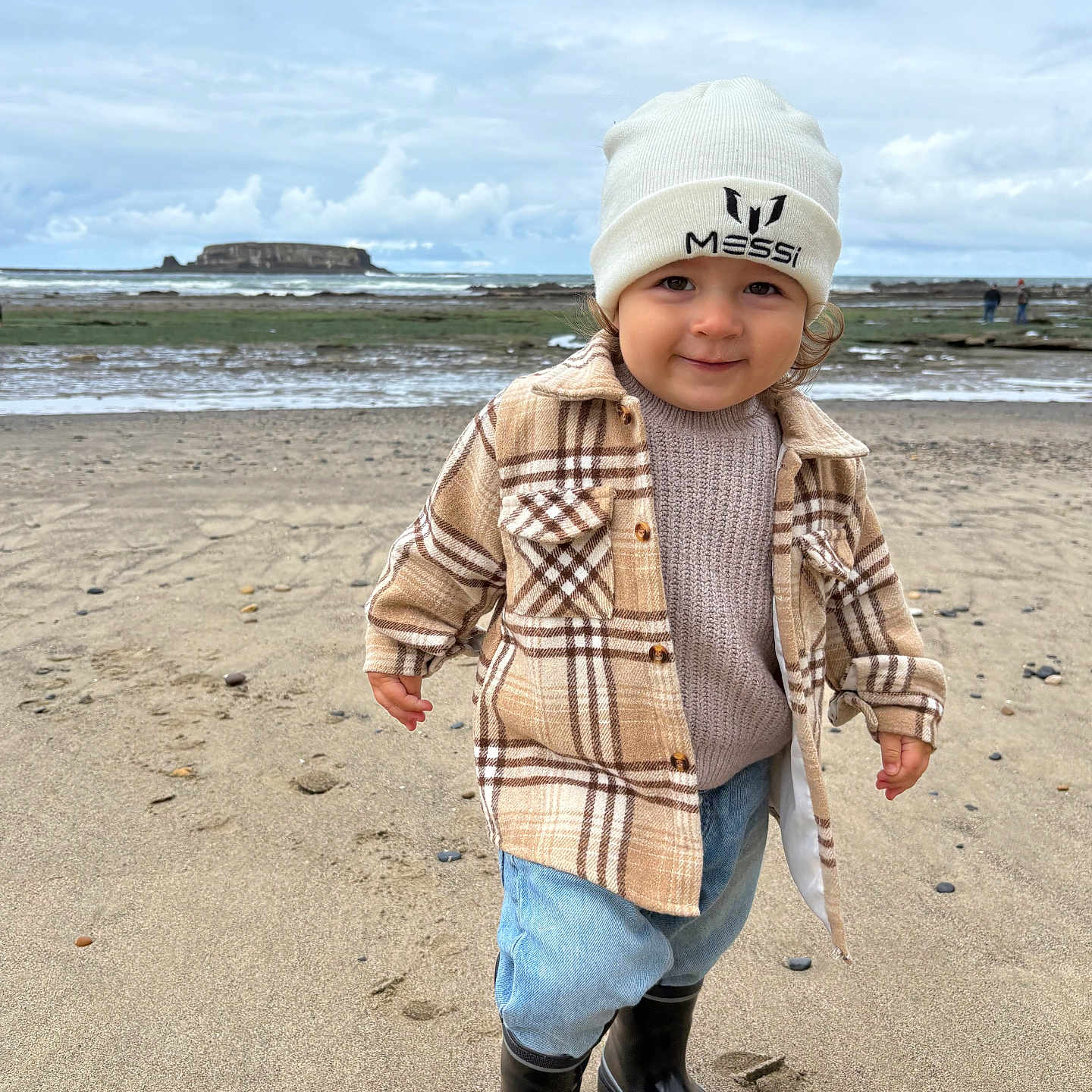 Ambrose joined the competition — help win amazing prizes! beach, beanie, boots, child, cloudy_sky, coast, curly_hair, footwear, jeans, nature, ocean, outdoor, person, plaid_jacket, portrait, sand, smile, sweater, toddler, water