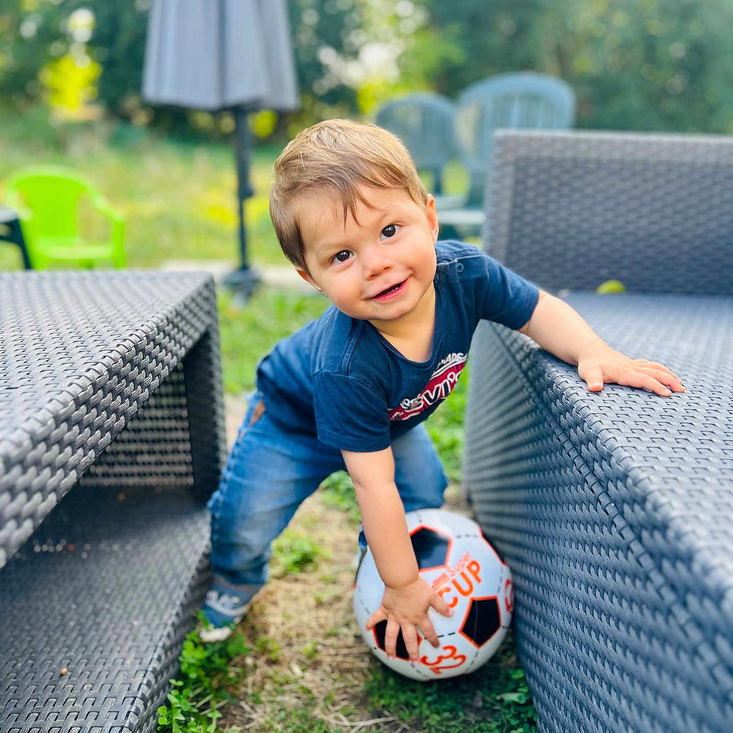 Raphaël participe au concours pour gagner de l'argent avec cette photo : blue_shirt, child, cute, daylight, fun, grass, greenery, happy, jeans, outdoor, patio_furniture, person, plastic_chair, playing, smiling, soccer_ball, toddler, umbrella, woven_chair, young_child