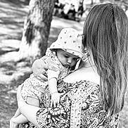 Ivanna a rejoint le concours — aidez-le/la à gagner de superbes lots ! baby, woman, holding, outdoor, tree, hat, patterned_dress, black_and_white, infant, nature, portrait, child, curious, sunhat, person, grass, daylight, hand, back_view, love