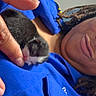 person, kitten, cat, sleeping, blue_shirt, hand, fingers, indoor, close_up, cute, tiny, black_and_white, pet, affection, cozy, gentle, dreadlocks, button, pocket, face_partial