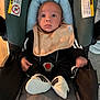 Noah is registered to the contest to win money with this photo: baby, car_seat, infant, child, footwear, sneakers, black_clothing, bib, seat_belt, indoor, person, cute, small_hands, wide_eyes, sitting, fabric, head_support, warning_labels, floor, straps