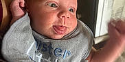 Noah is registered to the contest to win money with this photo: baby, infant, face, tongue_out, bib, clothing, arm, hand, person, indoor, expression, cute, child, skin, head, holding, smile, cheeks, human, newborn