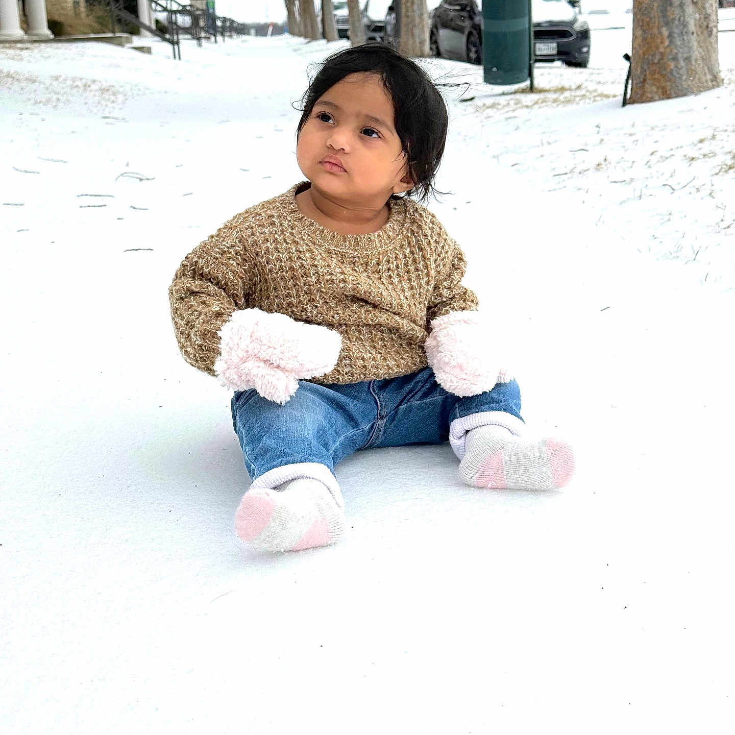 Dhrivi is registered to the contest to win money with this photo: toddler, child, snow, winter, outdoor, sitting, brown_sweater, mittens, socks, jeans, tree, car, sidewalk, winter_clothing, parked_car, nature, cold_weather, person, young_child, thoughtful