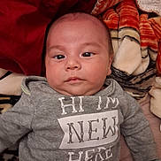 Andres joined the competition — help win amazing prizes! baby, infant, child, portrait, face, eyes, sitting, clothing, sweatshirt, blanket, bed, indoor, cozy, gray, red, text, name_tag, looking_at_camera, close_up, photography