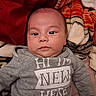 baby, infant, child, portrait, face, eyes, sitting, clothing, sweatshirt, blanket, bed, indoor, cozy, gray, red, text, name_tag, looking_at_camera, close_up, photography
