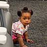 toddler, child, baby, crawling, portrait, face, pigtails, hair_bows, curious, serious_expression, indoors, carpet, floor, high_chair, furniture, pink_clothing, patterned_shirt, sitting, hands, daycare