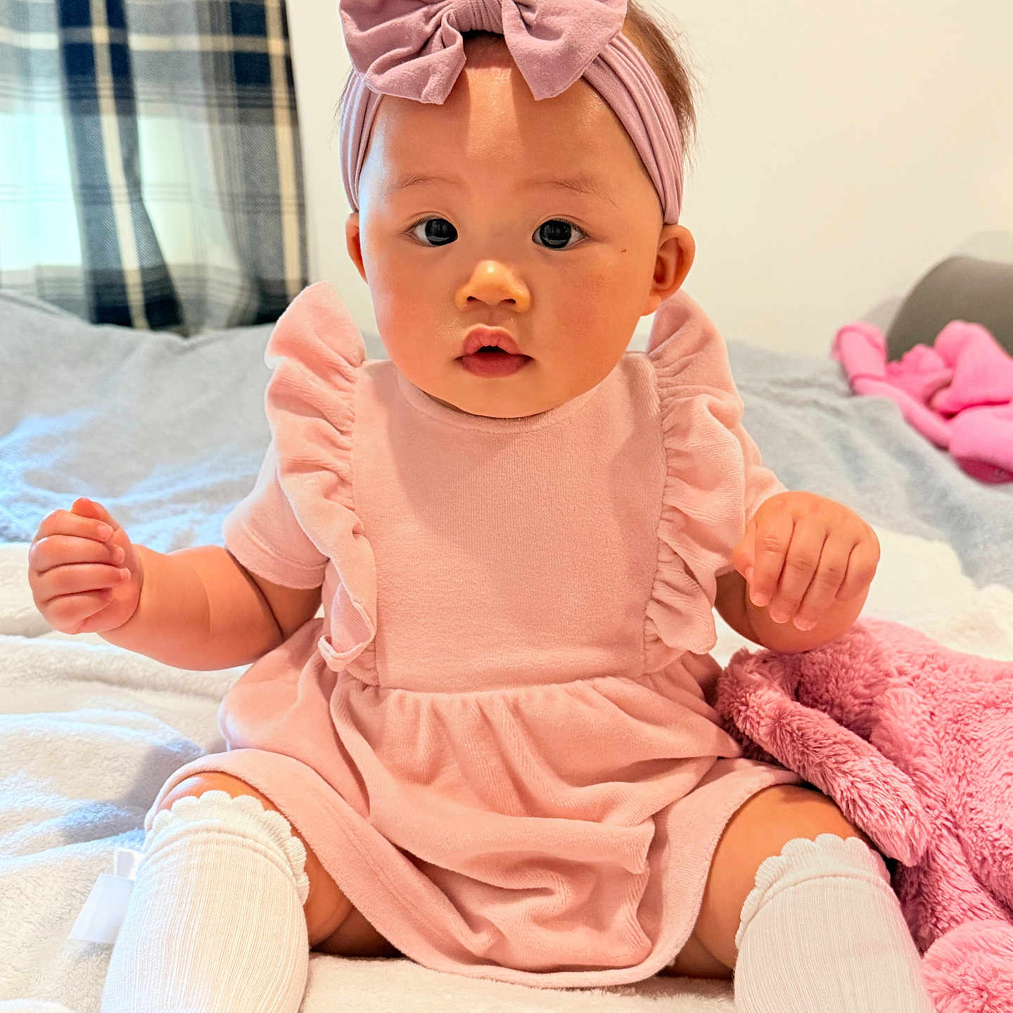 Orianna joined the competition — help win amazing prizes! baby, bed, blanket, bow, child, clothing, comfortable, curtains, cute, headband, indoors, infant, person, pink_dress, plush, portrait, room, sitting, socks, soft_lighting