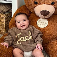 Jack is registered to the contest to win money with this photo: baby, child, teddy_bear, plush_toy, carpet, sweater, knitwear, smile, indoor, cozy, soft, cute, infant, person, hand, foot, furniture, blanket, room, happy