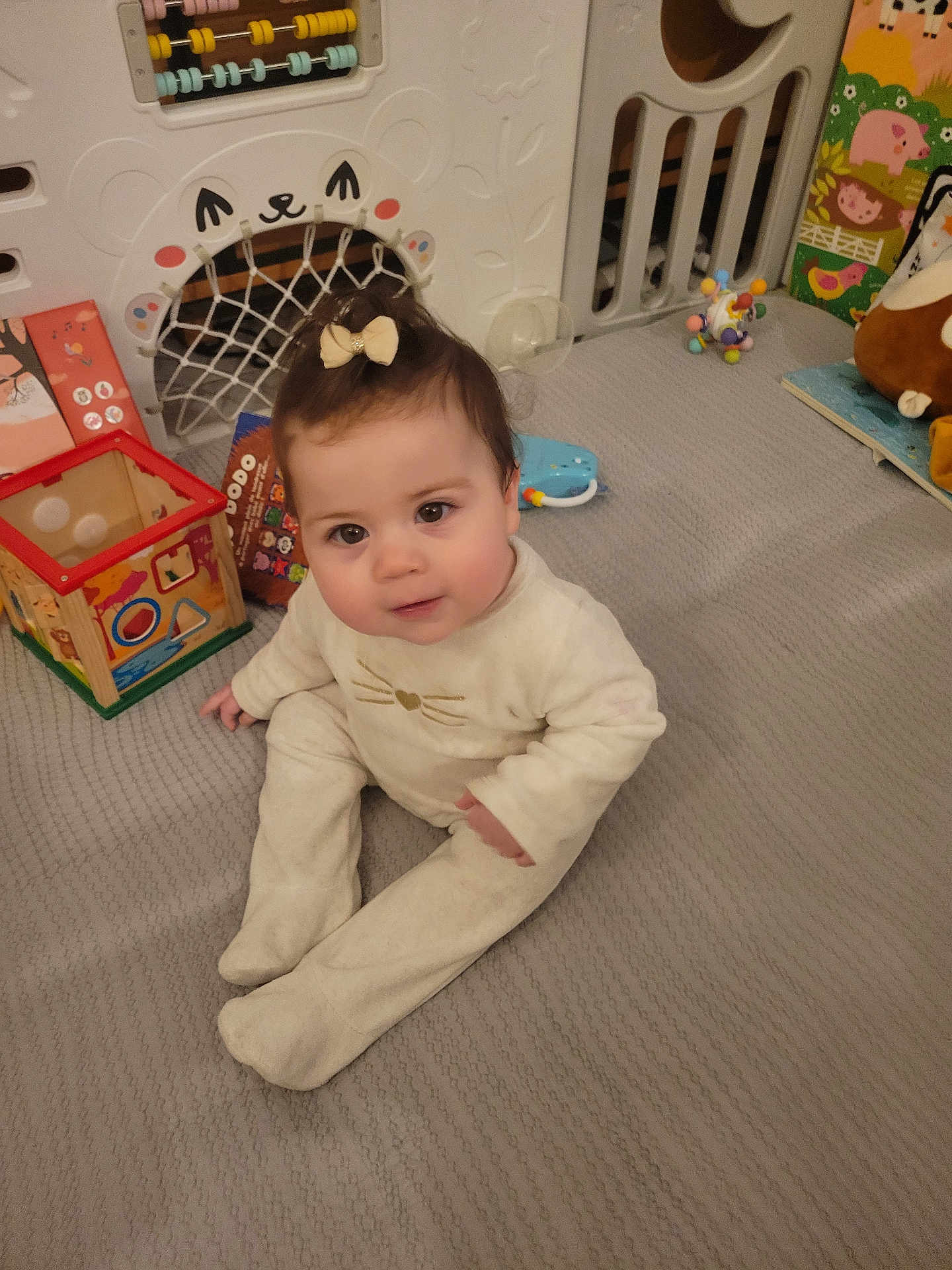 Ambre participe au concours pour gagner de l'argent avec cette photo : baby, infant, child, sitting, playroom, toy, activity_center, onesie, bow, face, eyes, cheeks, play_mat, indoor, plush_toy, crib, book, cute, portrait, floor