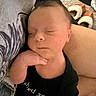 Weston is registered to the contest to win money with this photo: baby, newborn, sleeping, hand, face, person, arm, clothing, black_shirt, indoor, soft_light, cozy, carpet, slippers, resting, peaceful, closeup, portrait, cute, infant