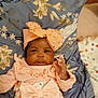baby, infant, child, pink_clothing, headband, bow, floral_pattern, cushion, blanket, hand, face, portrait, cute, indoors, soft_lighting, young_child, smile, person, resting, closeup