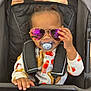 Rayven is registered to the contest to win money with this photo: toddler, child, pacifier, sunglasses, stroller, baby_clothes, seatbelt, hand, reflection, cute, smiling, indoors, portrait, fashion, infant, seat, colorful, young_child, person, casual