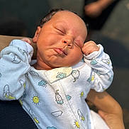 Orion is registered to the contest to win money with this photo: newborn, baby, sleeping, onesie, infant, hands, face, peaceful, patterned_clothing, person, closeup, soft_focus, cradled, outdoor, arm, cute, skin, expression, tiny, resting