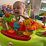 baby, child, infant, smiling, toys, activity_center, fisher_price, playful, indoor, nursery, stuffed_animals, furniture, floor, clothing, happy, legs, colorful, seat, baby_toys, fun