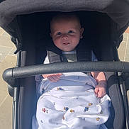 Archie is registered to the contest to win money with this photo: baby, blanket, stroller, child, infant, outdoor, sunlight, black, fabric, hand, face, seat, comfort, cute, person, portrait, clothing, head, expression, baby_stroller