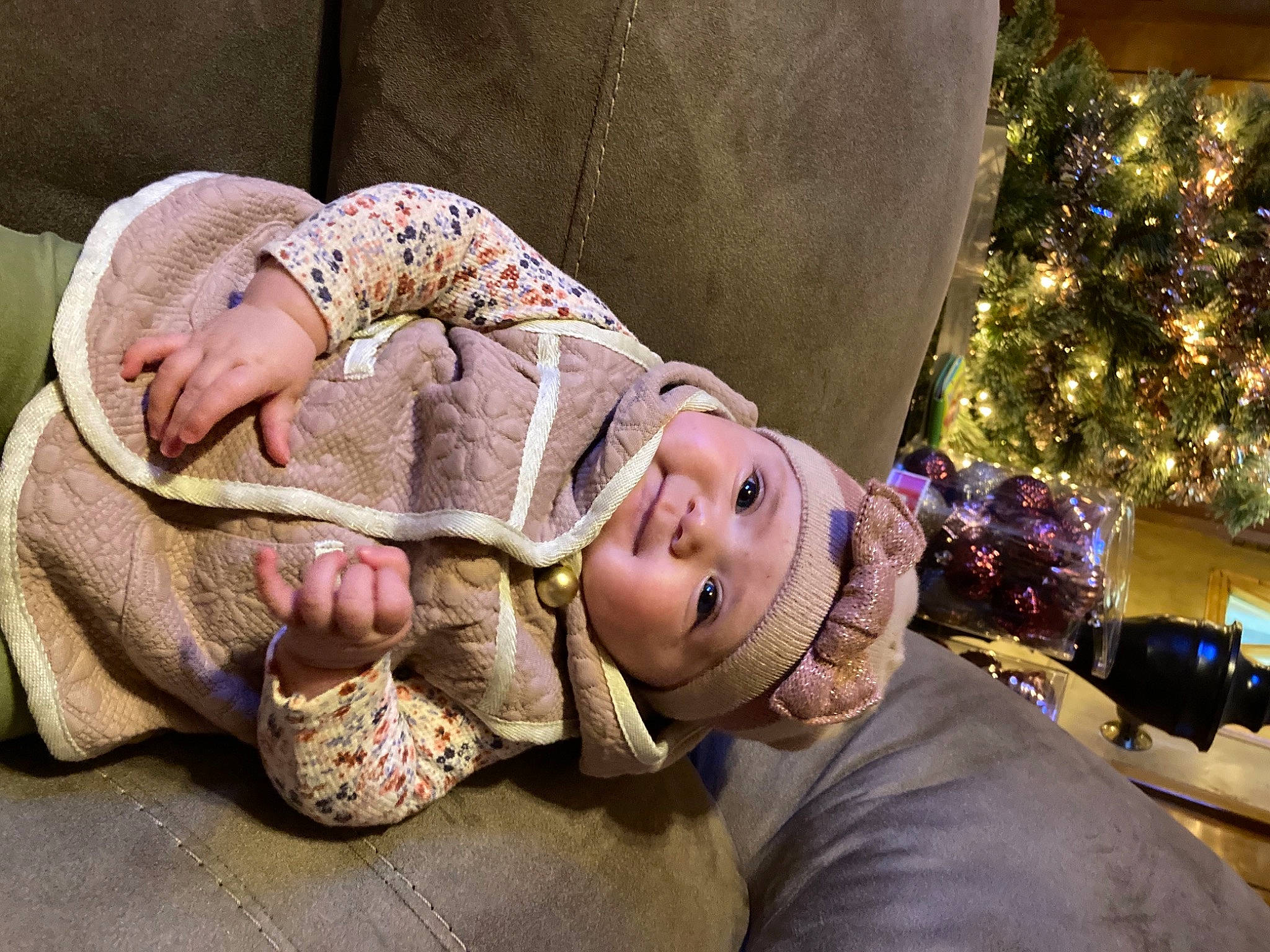 Kamila is registered to the contest to win money with this photo: baby, child, christmas_tree, comfort, event, facial_expression, fashion_accessory, fun, grass, happy, headwear, holiday, interaction, leg, leisure, person, plant, sitting, smile, toddler