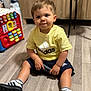 adidas, casual_clothing, child, comb, curious, floor, footwear, furniture, home, indoor, person, playtime, shorts, sitting, sneakers, toddler, toy, wooden_floor, yellow_shirt, young_child