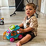 barefoot, blurred_background, casual_clothing, child, curious, expression, floor, furniture, home, indoor, kitchen, person, play, short_hair, sitting, toddler, toy, toy_car, wooden_floor, young_child