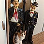 cat, statue, lamp_post, wooden_floor, cabinet, indoor, animal, decor, vintage, curious, posing, furniture, white, black, gray, flooring, two_figures, hat, tie, bow_tie