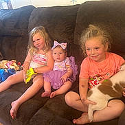 Avyanna is registered to the contest to win money with this photo: child, baby, couch, dog, toy, smile, indoor, child_playing, purple_dress, bow, snack, pet, happy, family, kids, home, casual, relaxed, furniture, living_room