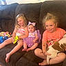 child, baby, couch, dog, toy, smile, indoor, child_playing, purple_dress, bow, snack, pet, happy, family, kids, home, casual, relaxed, furniture, living_room