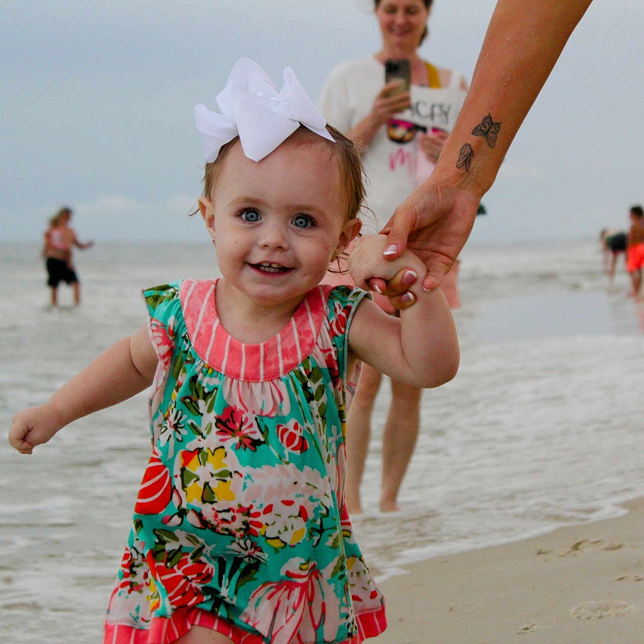 Berkleigh Grace joined the competition — help win amazing prizes! adult, background, beach, bow, child, cloudy_sky, colorful_dress, family, hand_holding, happy, legs, ocean, people, sand, shoreline, smiling, tattoo, toddler, vacation, water