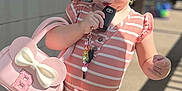 Berkleigh Grace is registered to the contest to win money with this photo: toddler, child, pink_purse, striped_clothing, outdoor, sunlight, shadows, car_key, hair_bow, footwear, curious_expression, standing, young_child, casual_clothing, playful, person, daylight, concrete_floor, decor, accessories