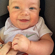 Julian is registered to the contest to win money with this photo: baby, infant, smiling, blue_eyes, onesie, hand, car_seat, cushion, person, child, cute, happy, skin, face, closeup, holding_hand, apparel, seat, cheeks, small