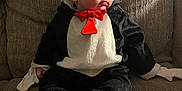 Julian joined the competition — help win amazing prizes! baby, child, penguin_costume, red_bow_tie, couch, beige, texture, seated, indoor, costume, cute, expression, curious, clothing, footwear, hands, head, face, person, soft_lighting