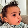 Bennett is registered to the contest to win money with this photo: baby, curly_hair, wide_eyes, onesie, patterned_clothing, couch, indoor, child, portrait, close_up, cute, infant, person, face, skin, expression, seated, young_child, cozy, curious
