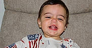 Bennett is registered to the contest to win money with this photo: toddler, child, smiling, happy, face, portrait, american_flag, shirt, clothing, indoors, couch, furniture, young_child, cute, baby, person, seated, expression, head, skin