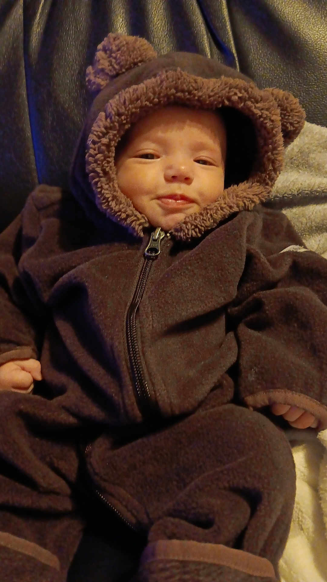Kahleal joined the competition — help win amazing prizes! baby, child, infant, fuzzy_clothing, brown, hood, bear_ears, zipper, smile, face, hand, sitting, blanket, leather, couch, warm_clothing, cute, indoors, portrait, comfort