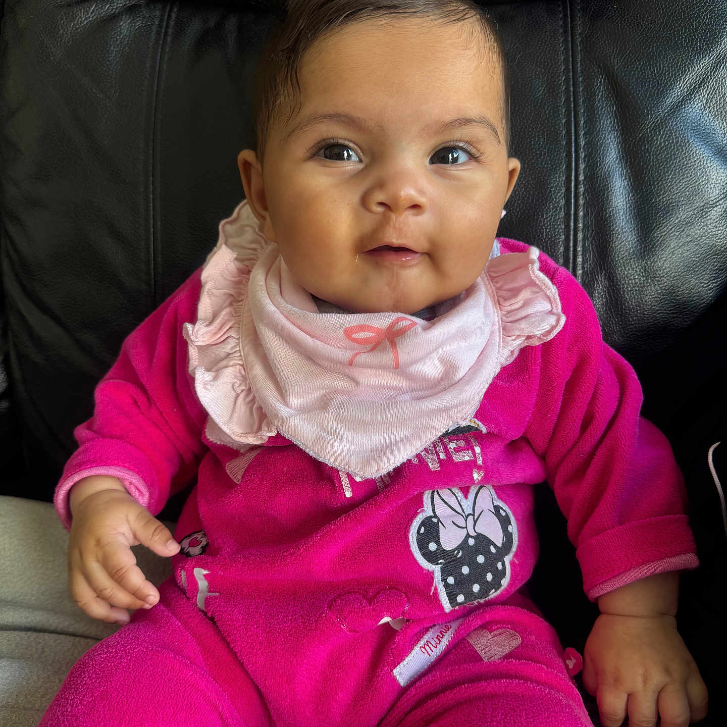 Aaliyah is registered to the contest to win money with this photo: baby, child, infant, pink_clothing, bib, minnie_mouse, sitting, leather_chair, cute, portrait, smiling, face, hand, indoors, young_child, happy, casual, cozy, comfortable, bright_colors