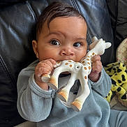 Aaliyah joined the competition — help win amazing prizes! baby, blue_clothing, child, closeup, cute, expression, face, giraffe, hands, home, indoor, infant, leather_couch, playing, plush_toy, remote_control, sitting, soft_toy, teething_toy, young_child