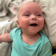 Archie is registered to the contest to win money with this photo: baby, infant, smile, happy, onesie, mint_green, lying_down, blanket, soft_texture, polka_dot, face, cheeks, cute, child, skin, expression, indoors, closeup, person, newborn