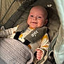 baby, smile, stroller, blanket, infant, clothing, cute, child, happy, face, seatbelt, fabric, knitted, indoors, person, newborn, soft, cozy, resting, small_hand