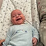 baby, smiling, onesie, light_blue, vehicles, changing_pad, star_pattern, happy, infant, child, cute, lying_down, indoor, soft_lighting, hand, fabric, person, face, small_child, joyful