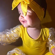 Leya a rejoint le concours — aidez-le/la à gagner de superbes lots ! child, baby, infant, headband, bow, yellow_outfit, smiling, profile_view, close_up, soft_lighting, bokeh, daisy_pattern, patterned_sleeves, sitting, cute, chubby_cheeks, portrait, warm_tones, fabric, adorable