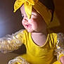 child, baby, infant, headband, bow, yellow_outfit, smiling, profile_view, close_up, soft_lighting, bokeh, daisy_pattern, patterned_sleeves, sitting, cute, chubby_cheeks, portrait, warm_tones, fabric, adorable